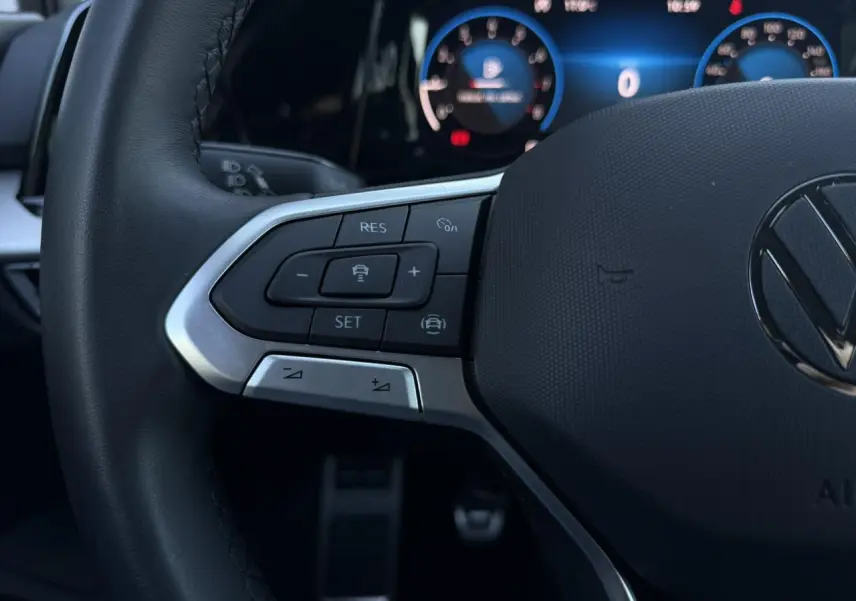 Gros plan sur le volant multifonction noir de la Volkswagen Golf 8 avec commandes intégrées et tableau de bord numérique en arrière-plan.