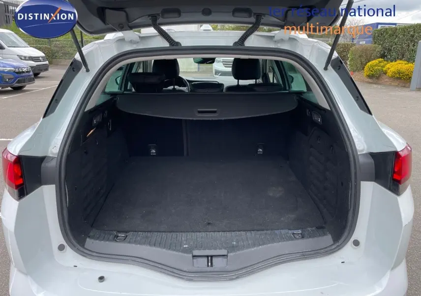 Vue arrière ouverte sur le coffre spacieux d’une Renault Mégane Break blanc glacier, intérieur noir et hayon relevé.