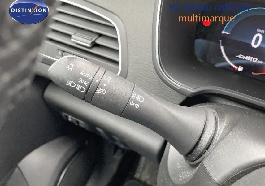 Gros plan sur la commande des phares à gauche du volant dans l’habitacle d’une Renault Mégane Break blanc glacier.