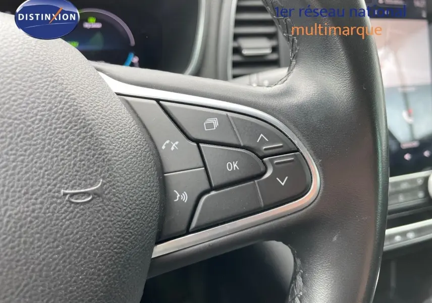 Gros plan sur les commandes au volant en cuir noir de la Renault Mégane Break blanc glacier, tableau de bord en arrière-plan.
