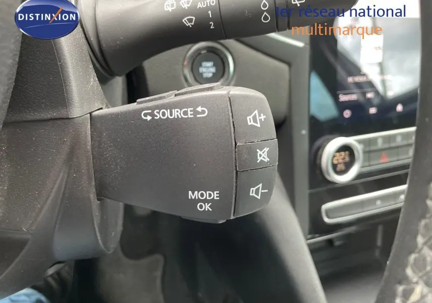 Gros plan sur la commande au volant de la Renault Mégane Break 1.6E-TECH 2021, avec tableau de bord et écran tactile en arrière-plan.