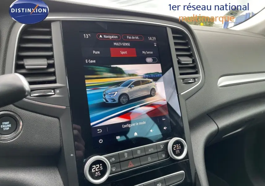Vue intérieure centrée sur l'écran tactile du tableau de bord affichant une Renault Mégane Break blanc glacier en mode sport.