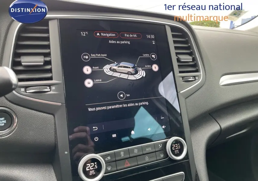 Vue intérieure du tableau de bord de la Renault Mégane Break blanc glacier, avec écran tactile et commandes de climatisation.