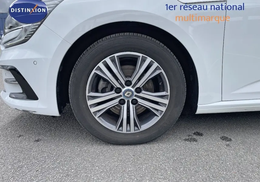 Gros plan sur la roue avant droite d’une Renault Mégane Break blanc glacier avec jante alliage distinctive.