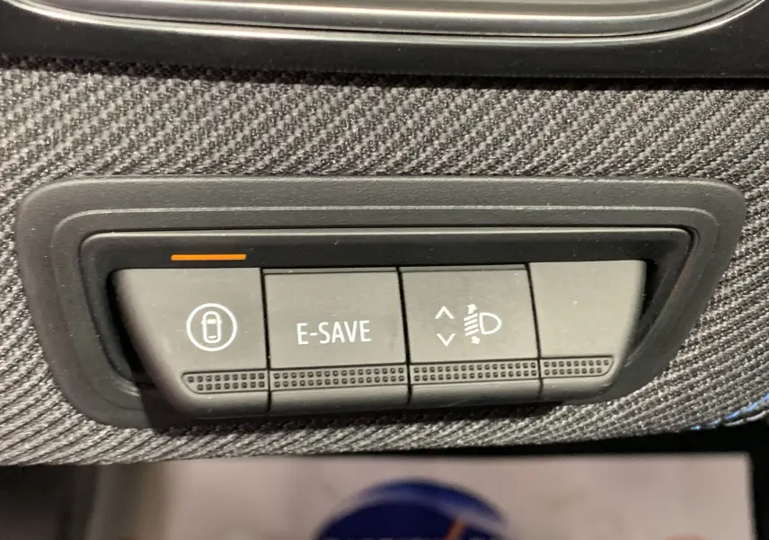 Gros plan sur les boutons de contrôle E-SAVE et réglage des phares sur la planche de bord en tissu du Renault Symbioz bleu iron.