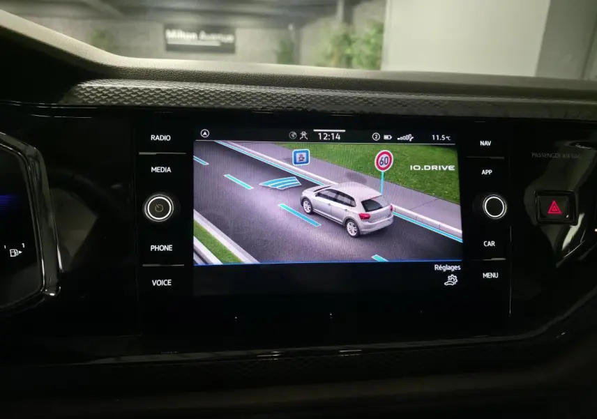 Écran tactile intérieur affichant la vue 3D d'une Volkswagen Polo grise en circulation avec indication de limitation de vitesse.