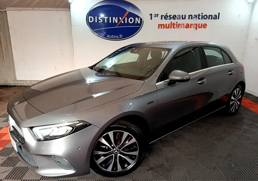 Vue 3/4 avant droit d'une Mercedes Classe A 250 e Business Line gris foncé avec phares LED allumés en intérieur showroom