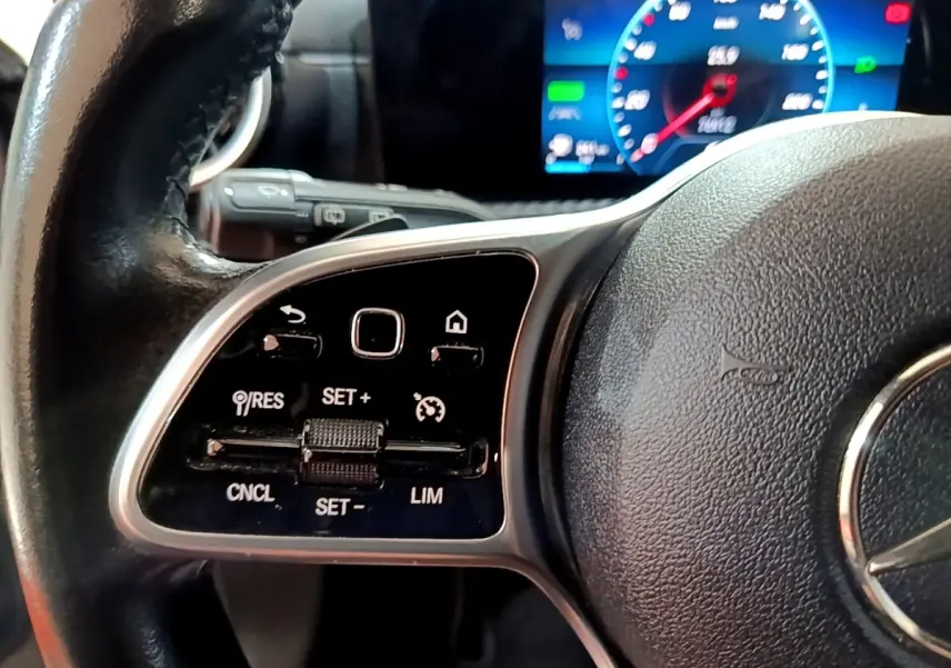 Gros plan sur le volant cuir noir de la Mercedes Classe A 250 e, avec commandes de régulateur et tableau de bord numérique bleu.