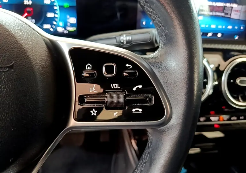 Gros plan sur le volant cuir noir côté gauche de la Mercedes Classe A 250 e avec commandes tactiles et tableau de bord digital.