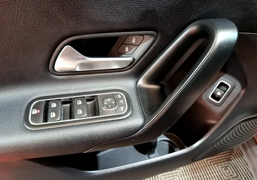 Gros plan sur la poignée intérieure et les commandes de porte côté gauche d'une Mercedes Classe A gris foncé.