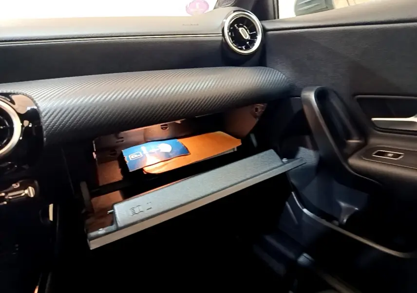 Gros plan sur la boîte à gants ouverte côté passager du Mercedes Classe A 250 e Business Line gris foncé, tableau de bord texturé.