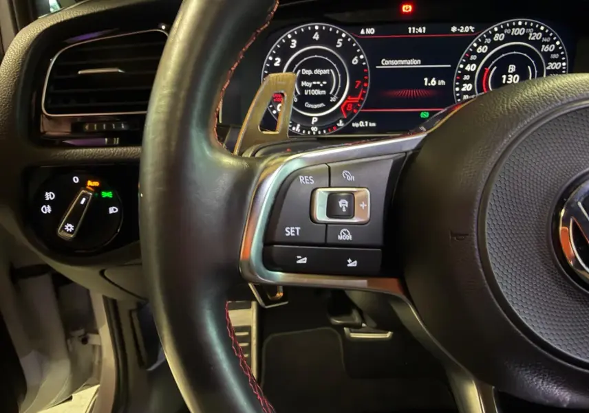 Gros plan sur le volant noir avec surpiqûres rouges et tableau de bord numérique de la Volkswagen Golf GTI Performance gris.