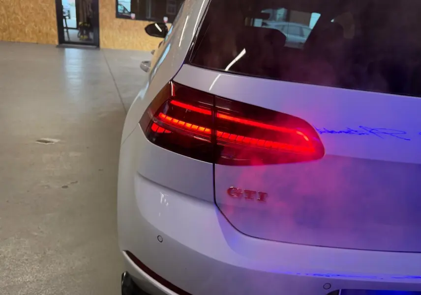 Vue arrière droite d'une Volkswagen Golf GTI Performance gris avec feux arrière LED allumés et logo GTI visible.