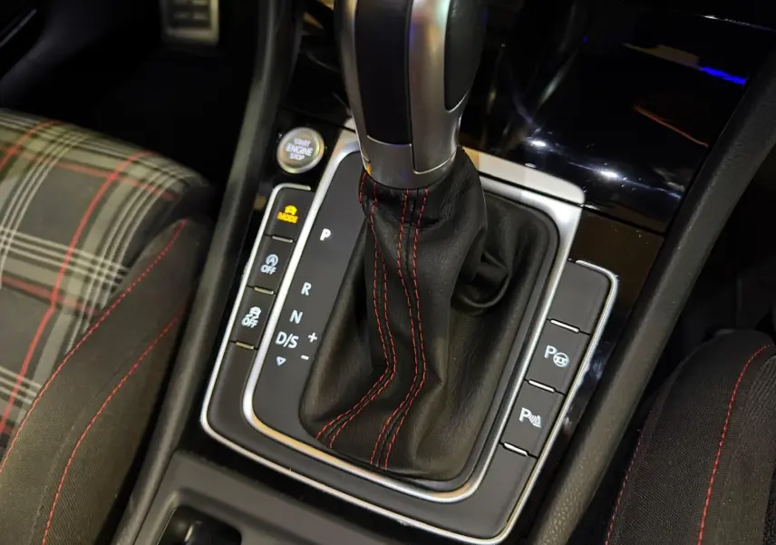 Gros plan sur la console centrale de la Volkswagen Golf GTI gris, avec levier de vitesse automatique et coutures rouges.
