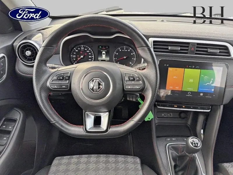 Vue intérieure centrée sur le volant cuir MG avec coutures rouges et écran tactile du MG ZS Cosmic Silver 2022.