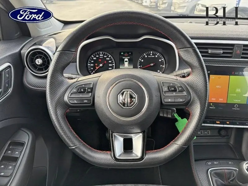 Vue intérieure centrée sur le volant cuir noir avec surpiqûres rouges du MG ZS Cosmic Silver, tableau de bord et écran tactile visibles.