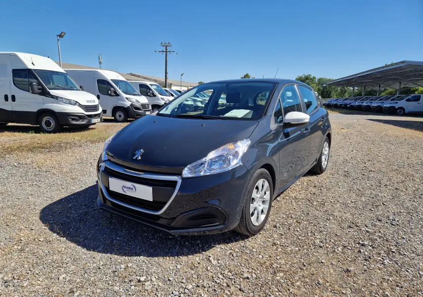 Peugeot 208 gris hurricane vue 3/4 avant droit, avec rétroviseurs blancs et jantes alliage, sur parking extérieur.
