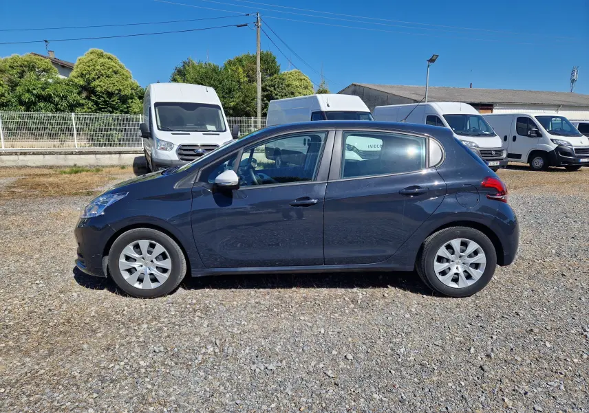 Peugeot 208 1.2 PureTech 68 en gris Hurricane vue de profil côté gauche sur un parking en gravier.