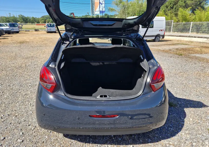 Vue arrière d'une Peugeot 208 gris hurricane de 2018 avec coffre ouvert sur un terrain extérieur ensoleillé.