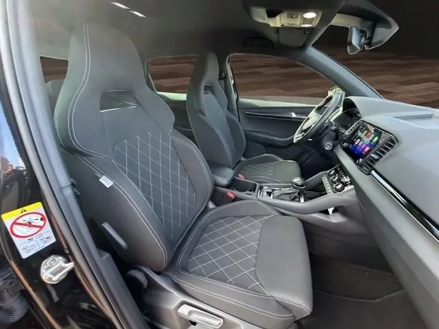 Vue intérieure côté gauche du Skoda Karoq noir 2025, sièges avant sport avec surpiqûres et tableau de bord moderne.