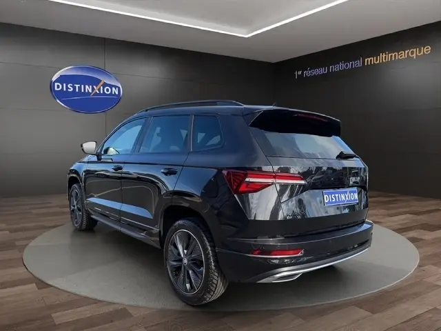 Vue 3/4 arrière droite d'un Skoda Karoq noir 2025 avec feux LED et jantes alliage foncé dans un showroom.