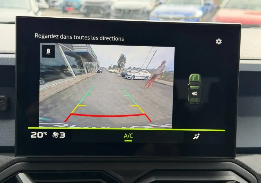 Écran tactile intérieur montrant la caméra de recul avec vue arrière sur une route et un piéton flou.