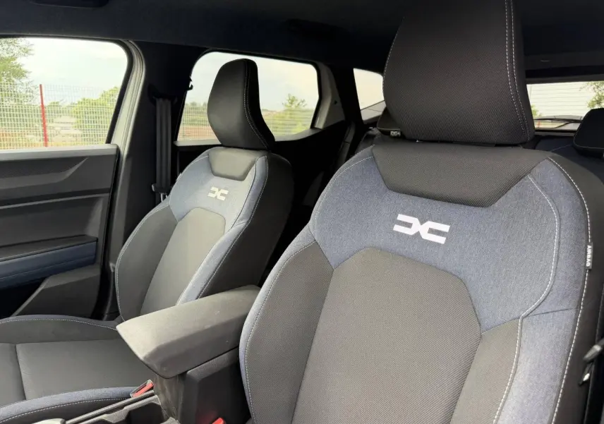Gros plan sur les sièges avant du Dacia Duster 2025 version Journey, tissu Denim avec logo réfléchissant et accoudoir central.