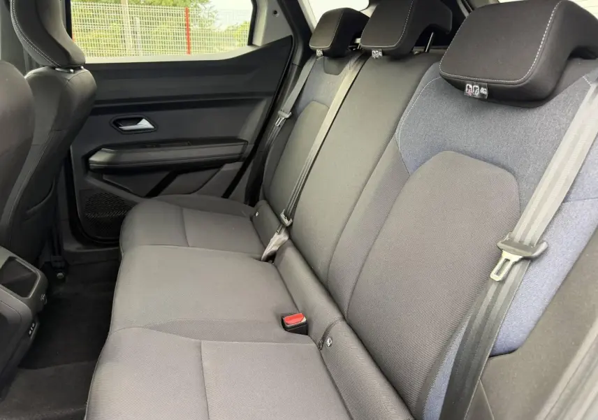 Vue latérale intérieure des sièges arrière gris foncé du Dacia Duster 2025, avec appuie-têtes et ceintures de sécurité visibles.