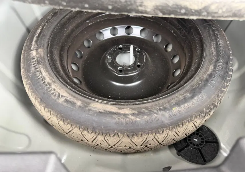 Vue rapprochée de la roue de secours noire dans le coffre gris clair du Dacia Duster 2025 Sandstone.