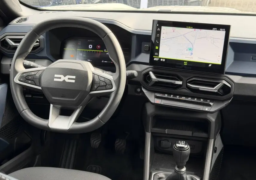 Vue intérieure frontale du tableau de bord du Dacia Duster 2025, avec volant multifonction, écran tactile et levier de vitesse manuel.