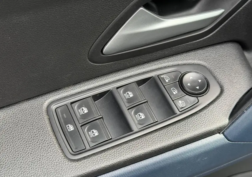 Gros plan sur les commandes des vitres électriques côté conducteur du Dacia Duster 2025 finition Journey couleur Sandstone.