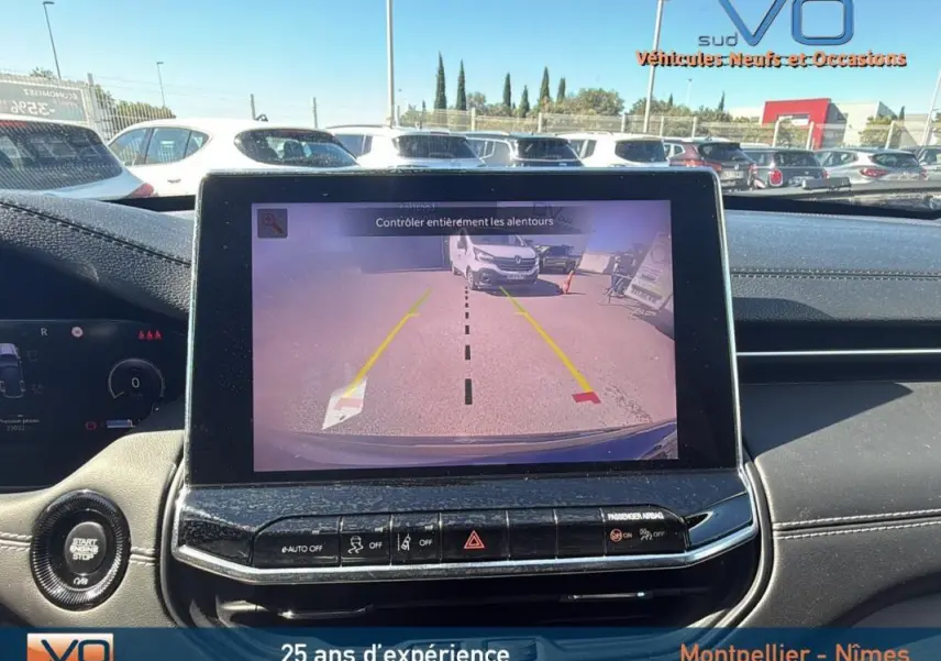Vue intérieure du tableau de bord du Jeep Compass gris 2023 avec écran tactile affichant la caméra de recul et commandes centrales visibles.