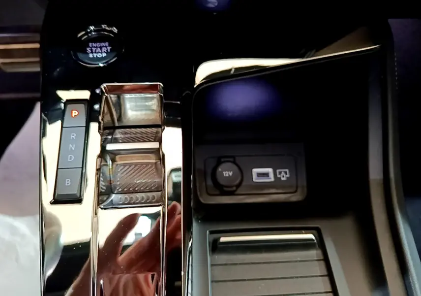 Gros plan sur la console centrale noire brillante de la Peugeot 308 PHEV 180 E-EAT8 GT avec levier de vitesses automatique et prise 12V.