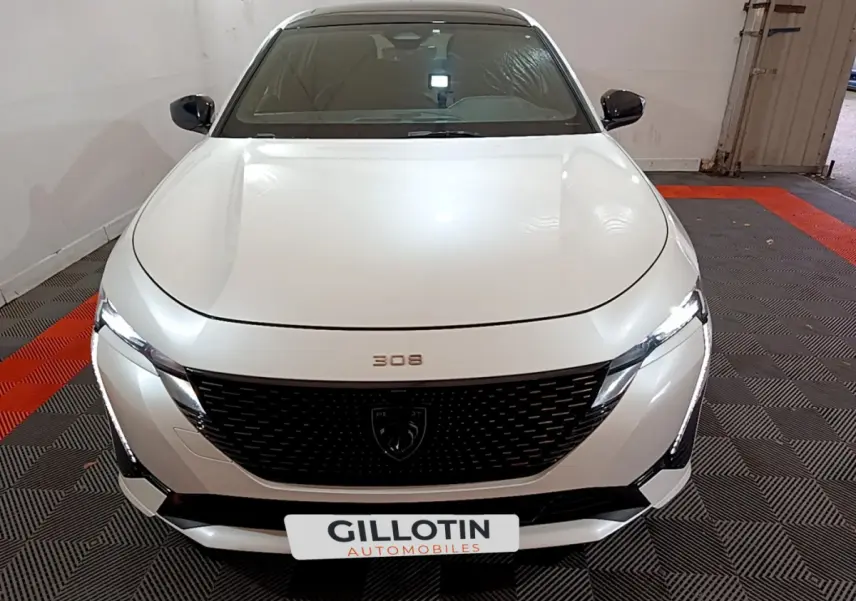 Vue frontale d'une Peugeot 308 PHEV 180 E-EAT8 GT blanche avec calandre noire et phares LED allumés.