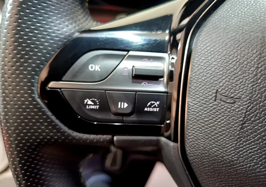 Gros plan sur les commandes gauche du volant cuir perforé du Peugeot 308 PHEV 180 E-EAT8 GT blanc de 2022.