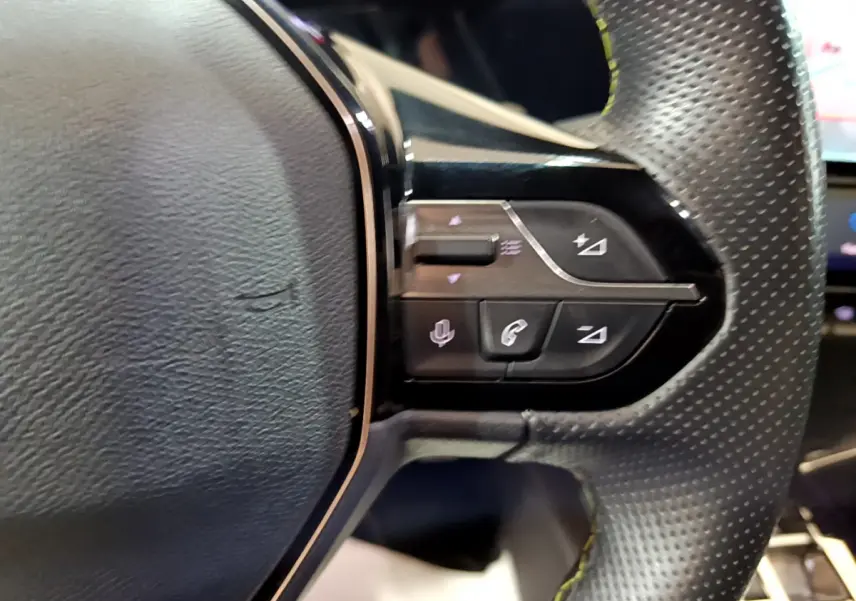 Gros plan sur les commandes du volant cuir perforé de la Peugeot 308 PHEV 180 E-EAT8 GT, boutons multifonctions noirs.