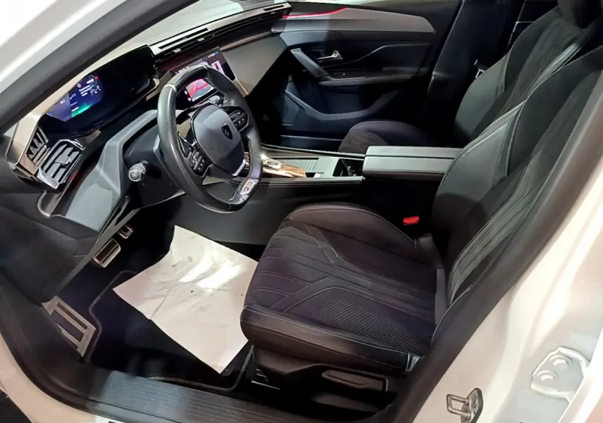 Intérieur côté conducteur du Peugeot 308 PHEV blanc, avec tableau de bord numérique et sièges noirs en tissu et cuir.