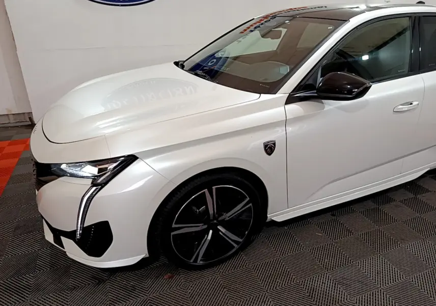 Vue 3/4 avant droite d'une Peugeot 308 PHEV 180 GT blanche avec jantes noires et logo GT sur aile avant.