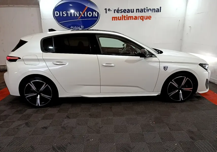 Peugeot 308 PHEV 180 E-EAT8 GT blanc vue de profil côté gauche en intérieur showroom avec jantes noires distinctives
