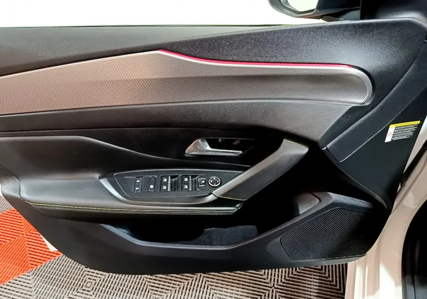 Gros plan sur la porte côté gauche d'une Peugeot 308 PHEV blanche, avec commandes électriques et surpiqûres vertes.