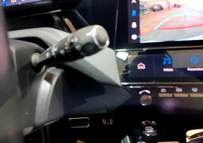 Gros plan sur la commande de clignotant et l'écran tactile affichant la caméra de recul dans l'habitacle noir d'une Peugeot 308 PHEV blanche.