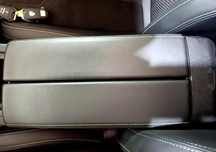 Vue rapprochée de l'accoudoir central noir avec surpiqûres vertes dans l'habitacle de la Peugeot 308 PHEV 180 GT blanche.