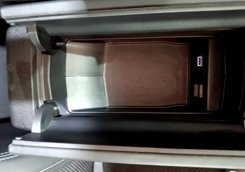 Vue rapprochée de la console centrale noire avec compartiment de rangement et port USB dans une Peugeot 308 PHEV 180 GT blanche.