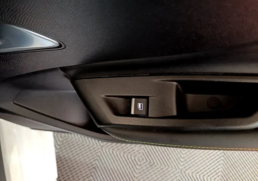 Gros plan sur la commande de lève-vitre côté conducteur dans l'intérieur noir de la Peugeot 308 PHEV 180 GT blanche.