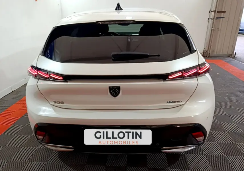 Vue arrière d'une Peugeot 308 PHEV blanche avec feux LED allumés dans un garage showroom.
