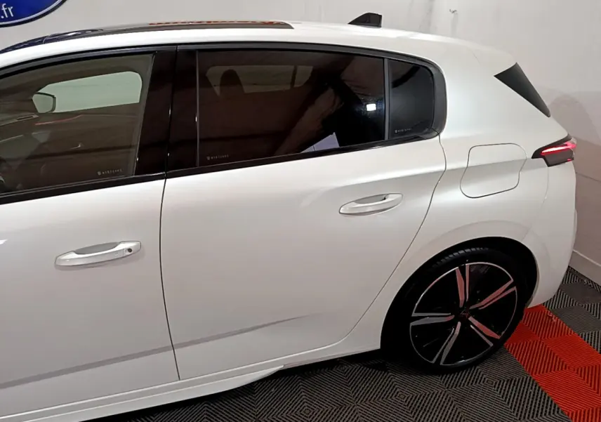 Vue latérale droite d'une Peugeot 308 PHEV 180 E-EAT8 GT blanche avec jantes noires et vitres teintées.