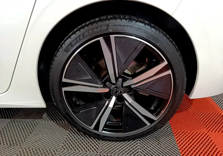 Gros plan sur la roue avant droite noire et argentée du Peugeot 308 PHEV blanc, soulignant la jante au design moderne.