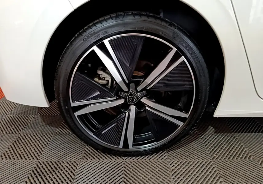 Gros plan sur la roue avant droite d'une Peugeot 308 PHEV 180 E-EAT8 GT blanche avec jante alliage noire et argentée.