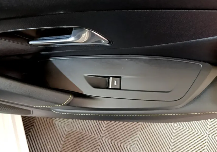 Bouton de commande de lève-vitre sur la porte intérieure côté gauche d'une Peugeot 308 PHEV blanche.