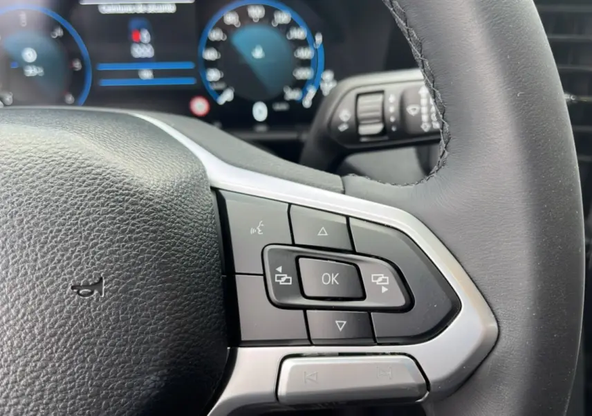 Gros plan sur le volant cuir multifonctions du Volkswagen Amarok noir, avec commandes intégrées et tableau de bord numérique flou en arrière-plan.